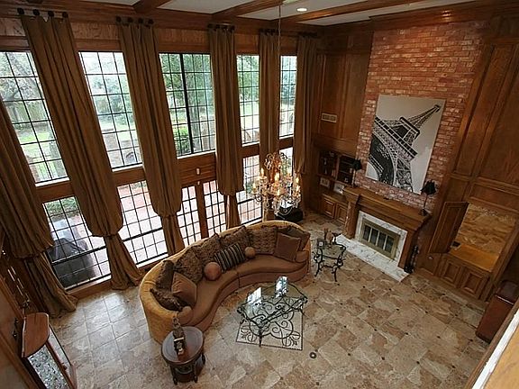 The two story fireplace is beautifully enhanced w/ marble & brick, plus custom mantle. To the left is shelving & to the right is a pass-through for the wet bar. There are two sets of French doors (one leads to outdoor courtyard & other to the study).