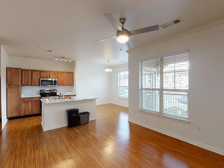 Apartment kitchen with stainless steel appliances, wood-style flooring, and marble-style countertops (shown here). Quartz-style countertops are available in select homes.