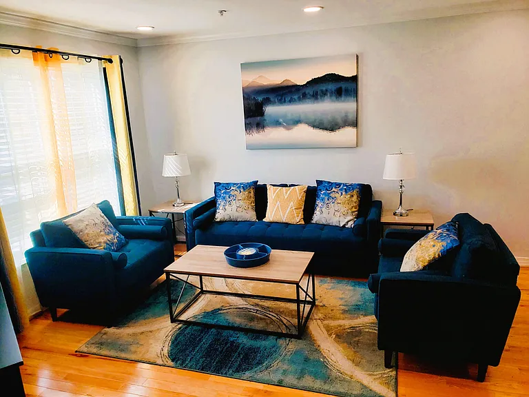 Comfortable living room with sofa seating, side tables, and a coffee table, plus a large window with blinds.