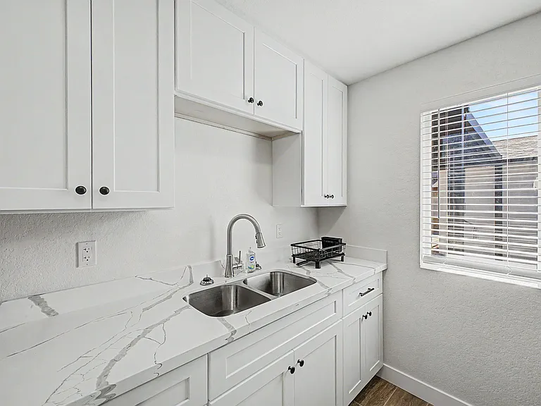 Clean kitchen workspace with ample white cabinetry, double-basin sink, and durable countertop beside a window.