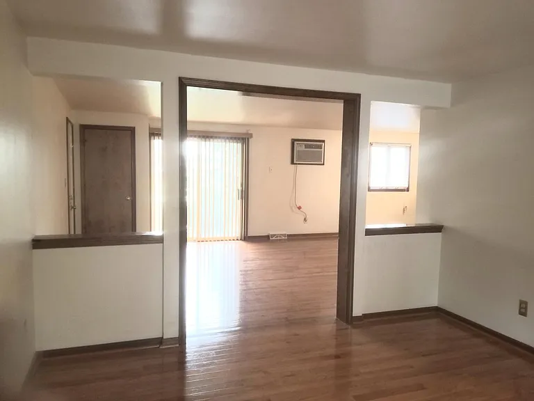 From the diningroom, looking at the living room and kitchen dining area. Wall air-conditioning unit. Patio door has vertical blinds. All genuine hardwood floors.