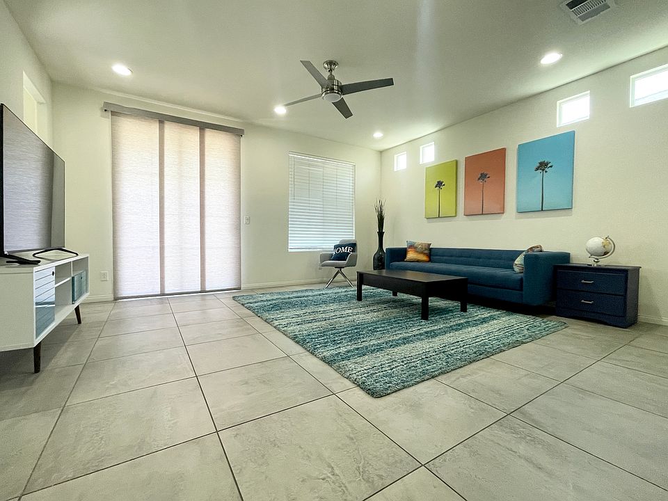 The fun and funky fully-furnished living room has a ceiling fan, sofa, chairs, end table, 65in TV, access to the balcony, and a view of the kitchen!