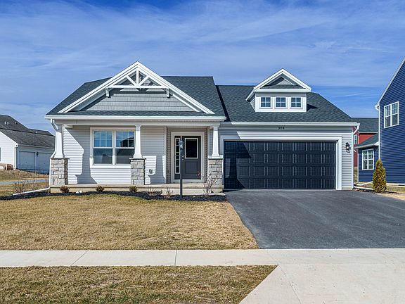 Front view of a single-story home with light siding, stone accents, covered porch, black garage door