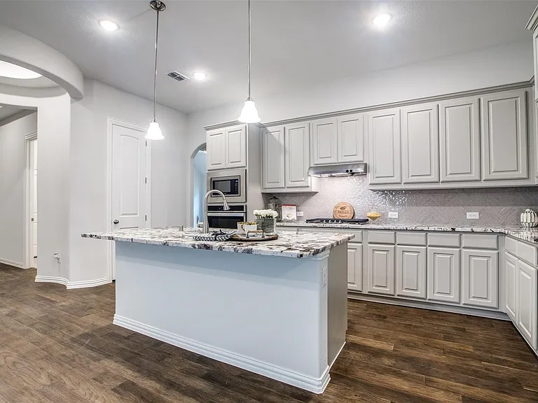 Contemporary kitchen featuring wood-finish flooring, a central island with a stone countertop, pendant lighting, shaker-style cabinetry, and a patterned backsplash