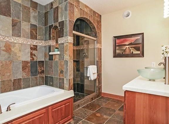 Main level master spa-like bathroom. Custom arches in mobi slate tile shower. Seperate soaking tub w/ jets. Limestone his/hers vanity w/ vessel sinks. Speakers in ceiling stay!!