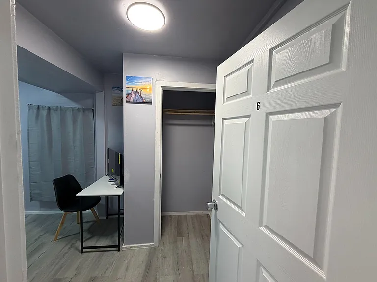 Private room area with a desk/workspace and an open closet nook, finished with durable flooring and overhead lighting.