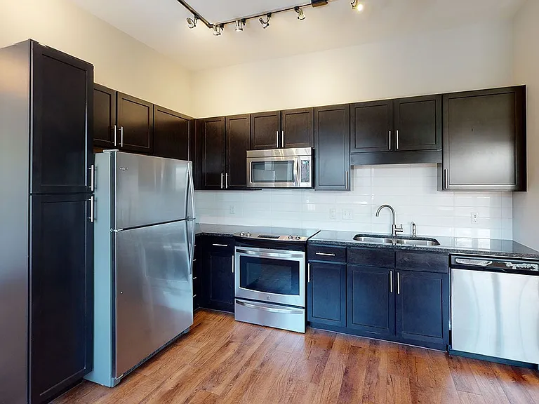 Apartment kitchen with stainless steel appliances, granite countertops and wood-style flooring.