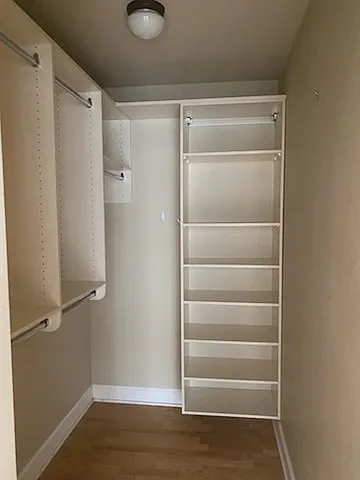 Walk in closet for second bedroom is spacious and includes dressing rods and organizational bins.