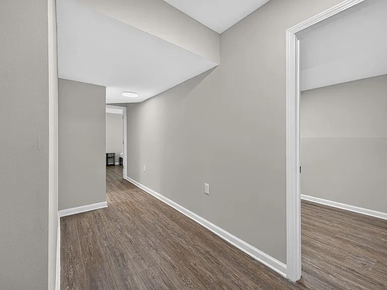 Wide hallway with wood-look flooring and neutral walls, offering easy access to adjacent rooms and flexible wall space.