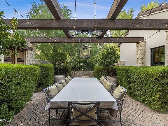 Elegant courtyard dining area with pergola, cafe lighting, and a tranquil garden setting.