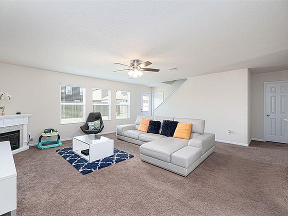 Warm and inviting living room featuring high ceilings, dark stained ceiling fan with lighting, large windows providing natural lights throughout, custom paint, fireplace, and plush carpet.