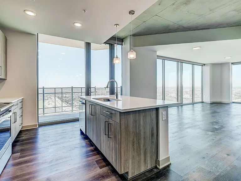 Stunning open kitchen and living room concept with stainless steel appliances, wood plank flooring, pendant lighting and quartz countertops