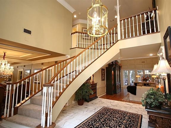 WIDE OPEN FOYER SHOWS ELEGANCE AND CLASS. The large entry way showcases white and gray marble flooring, a graceful staircase and the oversized living area beyond that overlooks a romantic setting in a tremendous backyard.