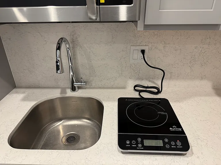 Closer view of single burner induction cooktop, sink and faucet.