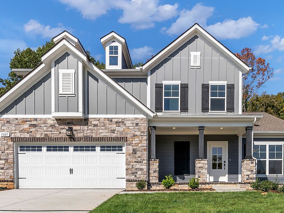 Elegant farmhouse with rustic wood shutters, sleek dark siding, and timeless stone accents in Brush