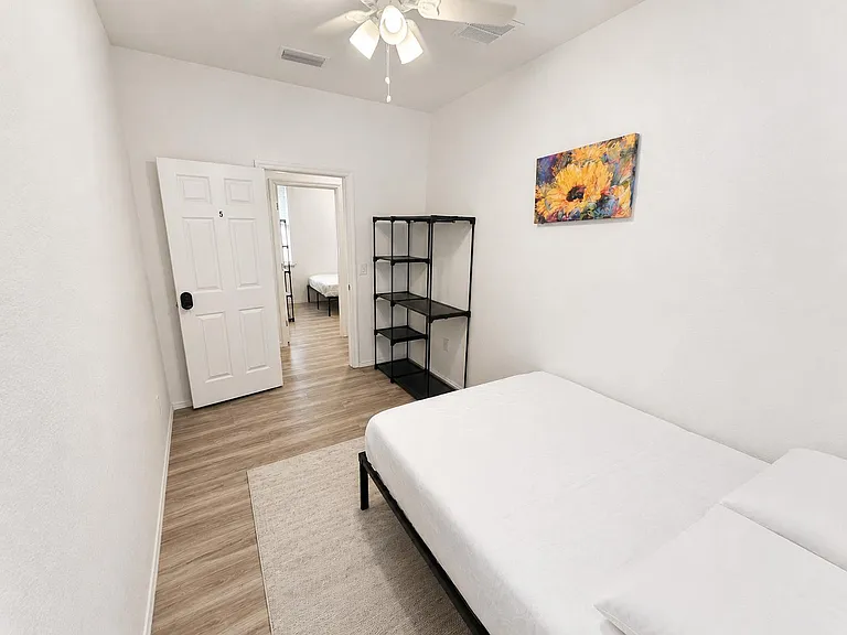 Private bedroom with wood-look flooring, ceiling fan, bed, and open shelving for easy storage and organization.