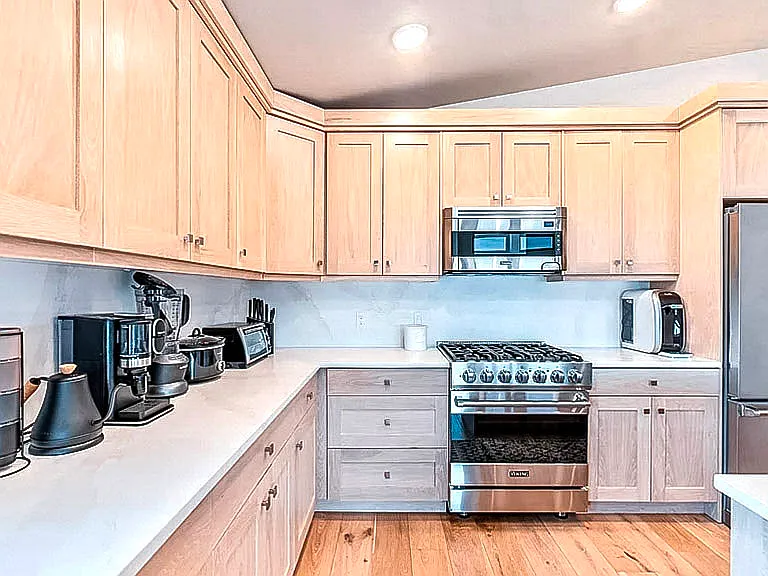 Fully equipped kitchen with light wood cabinetry, stainless steel appliances, and gas range