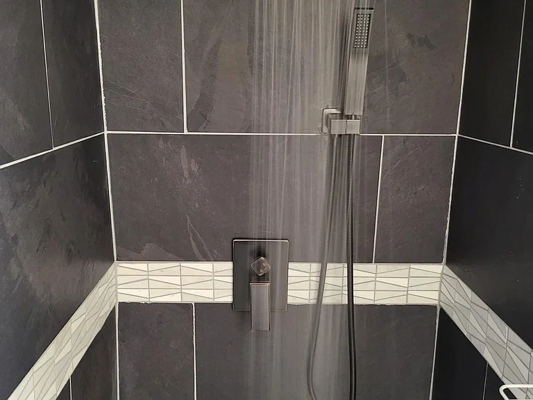 Second smaller bathroom with rain shower, hand spray, and a beautiful wrap around tile with decorative strip, and caddy for shampoo, conditioner...
