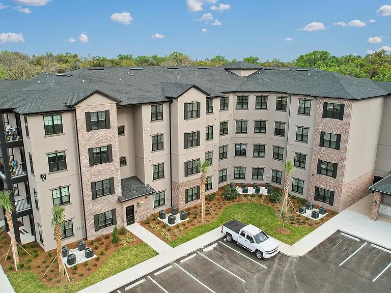 Charming apartment complex with modern brick and stucco facade, surrounded by lush greenery and ample parking, offering a tranquil and inviting living environment.