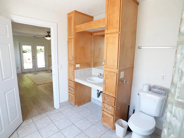 Bathroom with tiled floors, vanity sink with extensive built-in cabinetry, and convenient access to adjacent living area.