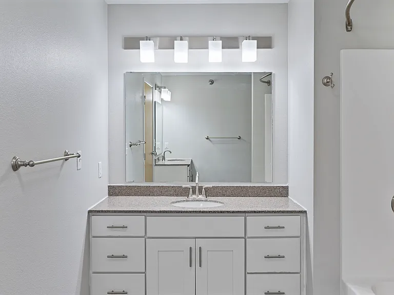Elegant bathroom with sleek white cabinetry, modern light fixtures, and a spacious mirror above a granite countertop. Elegant bathroom with sleek white cabinetry, modern light fixtures, and a spacious mirror above a granite countertop.