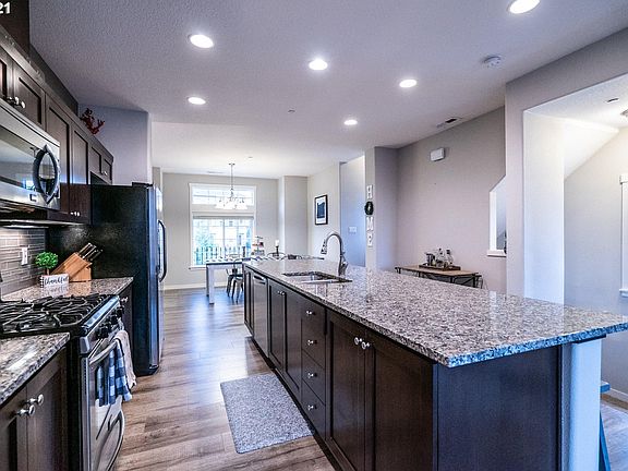 Kitchen with large island, granite counters, stainless steel appliances and luxury vinyl plank wood flooring.