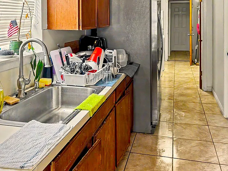 Galley-style kitchen with ample wood cabinetry, full-size refrigerator, and a double-basin sink beside a window.