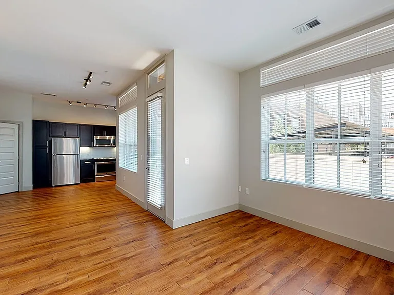 Apartment kitchen with stainless steel appliances, dining and living room with wood-style flooring.