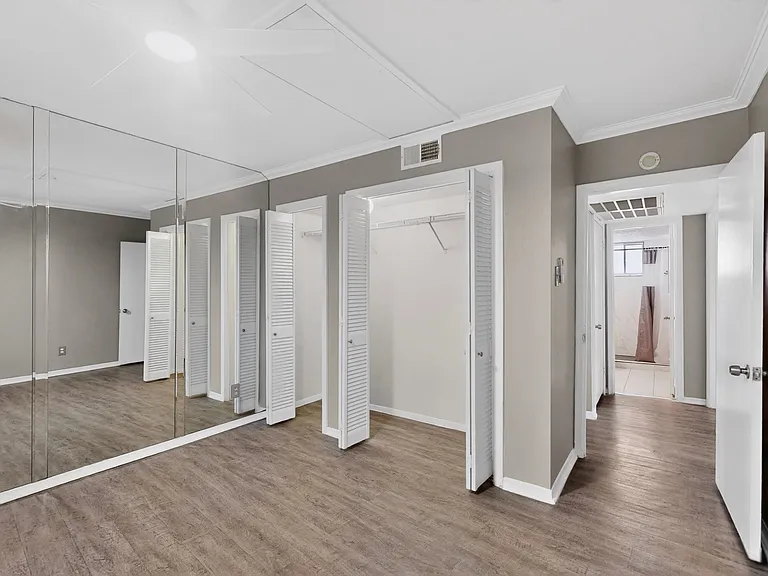A bedroom featuring a wide built-in closet with inner lighting and a mirror wall reflecting the space