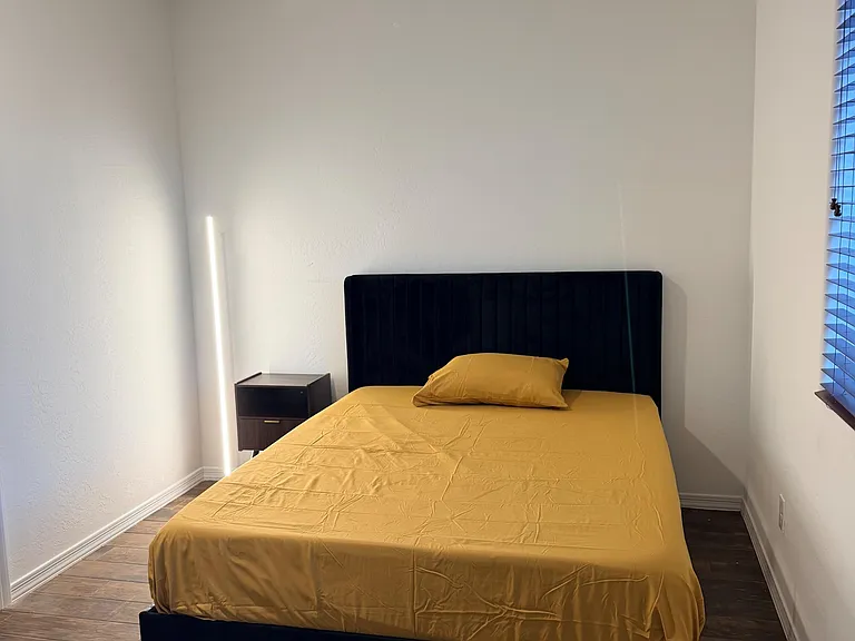 Furnished bedroom with a Queen-size bed, nightstand, and wood-look flooring, plus window blinds for light control.