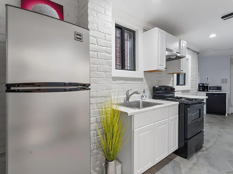 Galley-style kitchen with white cabinetry, stainless refrigerator, gas range, and sink, plus durable tile flooring.