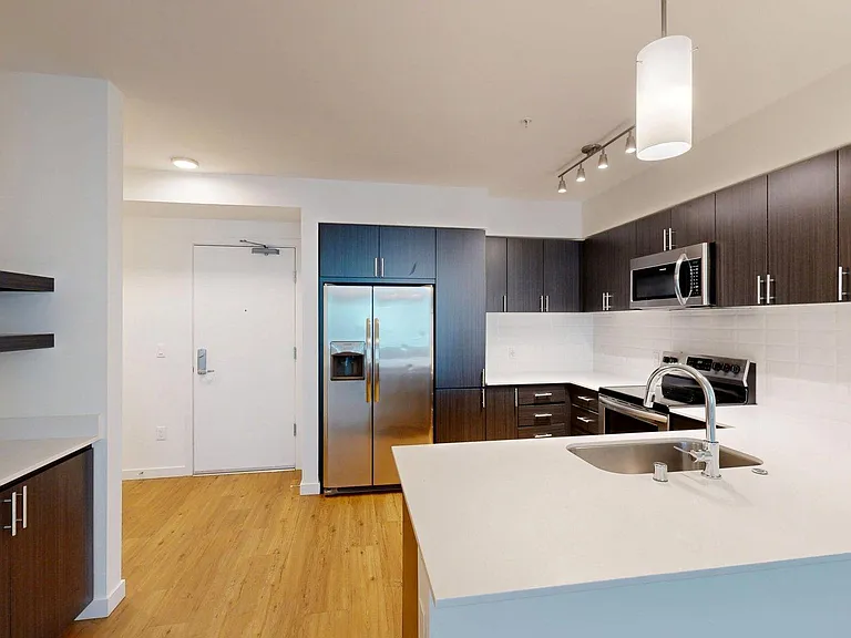 Apartment kitchen with stainless steel appliances, light counters, and wood style floor.