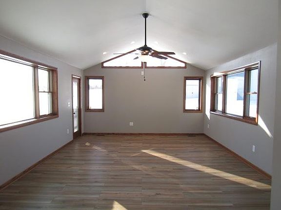 Great room has faux wood floors, gray walls, natural wood trim, door to patio, and ceiling fan plus 4 spotlights.