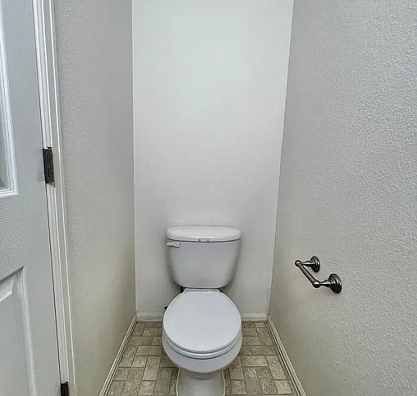 Powder room contains a toilet, sink, large mirror, and cabinets. It is located just opposite the garage entry door, and across from the kitchen bar area.