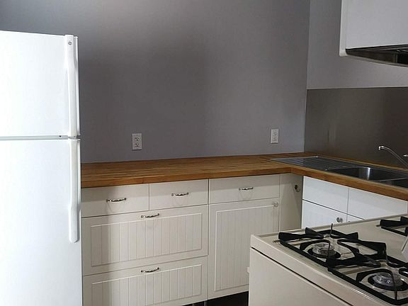 Kitchen as seen from doorway. Refrigerator, cabinets with butcher block counters, sink, stove, microwave