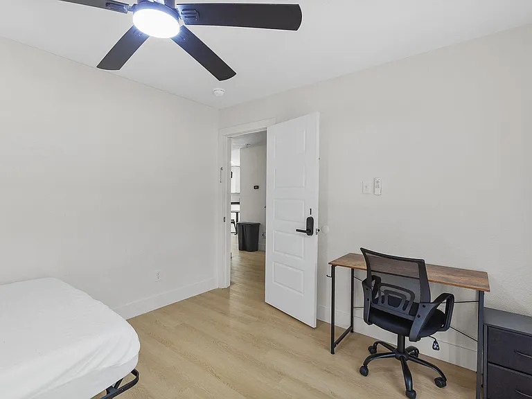 Private bedroom with a ceiling fan, wood-style flooring, and a dedicated desk area for work or study.