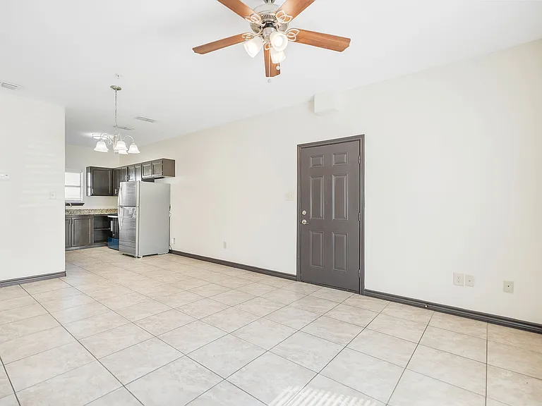 Interior view of a large, empty room with tile flooring and a ceiling fan at La Joya Apartments in Laredo, Texas