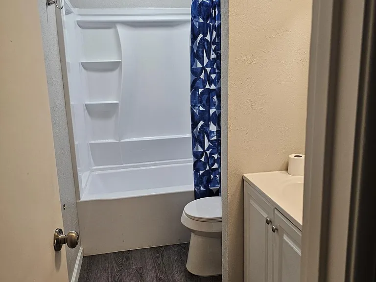 Full bathroom with a single-sink vanity, framed mirror, and tub/shower combo with curtain, plus durable wood-look flooring.