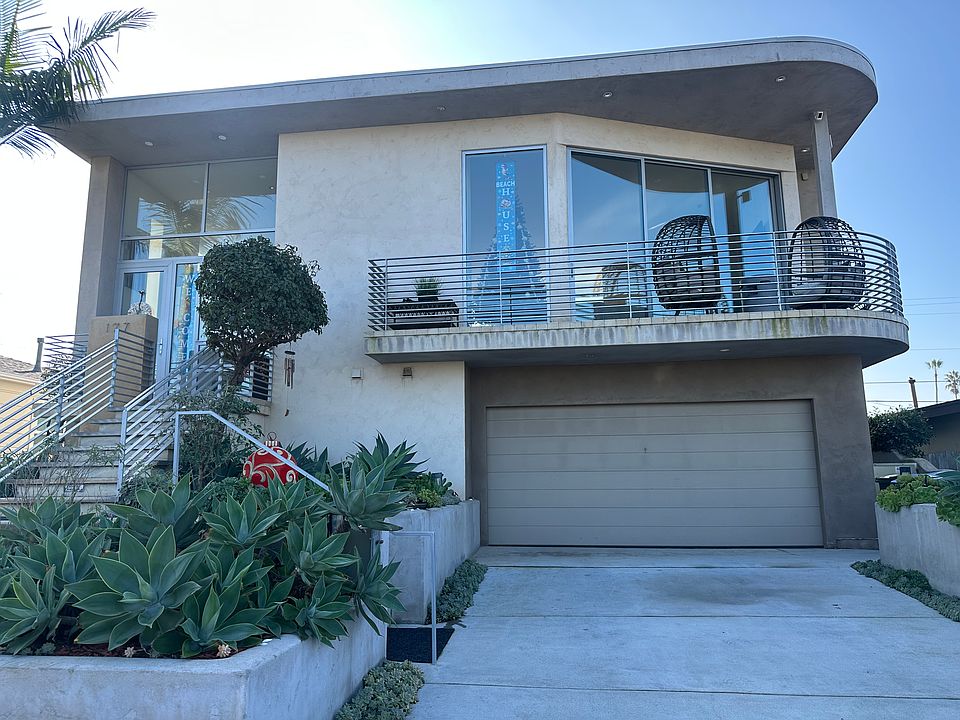 Front of house with mid-level entry, two-car garage with 240-V charging outlet, and balcony.