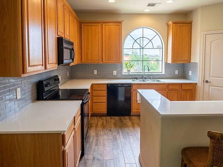 Open kitchen with large arched window, granite countertops, tile backsplash, stainless appliances, breakfast bar and abundant light coming from the arched window