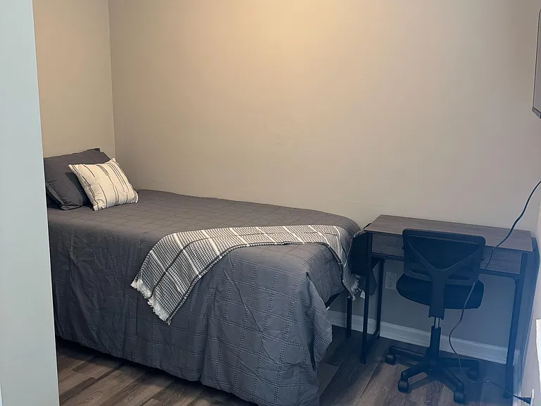 Private bedroom with a twin bed, ceiling fan, nightstand, and a work desk for comfortable daily living.