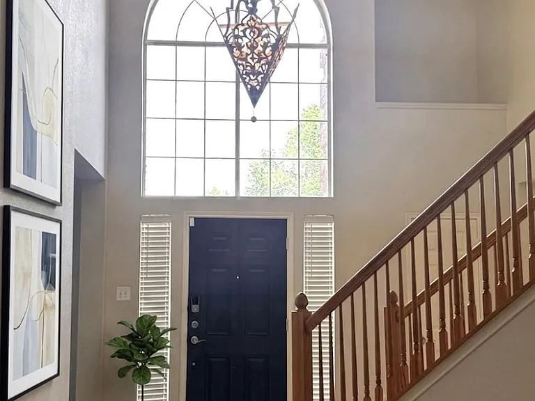 Grand entryway featuring a tall arched window, a dark paneled door, and a staircase with wood railing and balusters