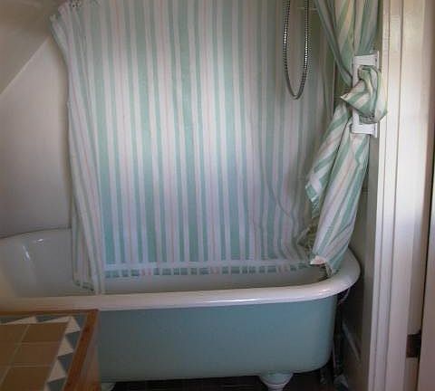 View of tub/shower in bathroom. Partial view of sink and cabinet. Toilet at opposite end of this room below small north window.
