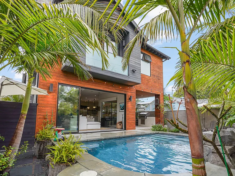 View of the living room from the verdant backyard oasis with heated pool, firepit and patio