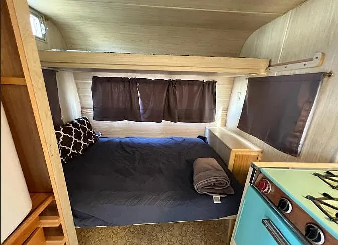 Compact sleeping nook with a full-size bed, privacy curtains, and built-in shelving for personal storage.