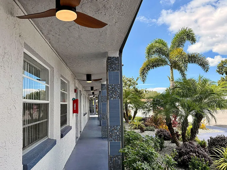Charming apartment exterior with modern ceilings, lush landscaping, and tall palm trees under a bright blue sky.