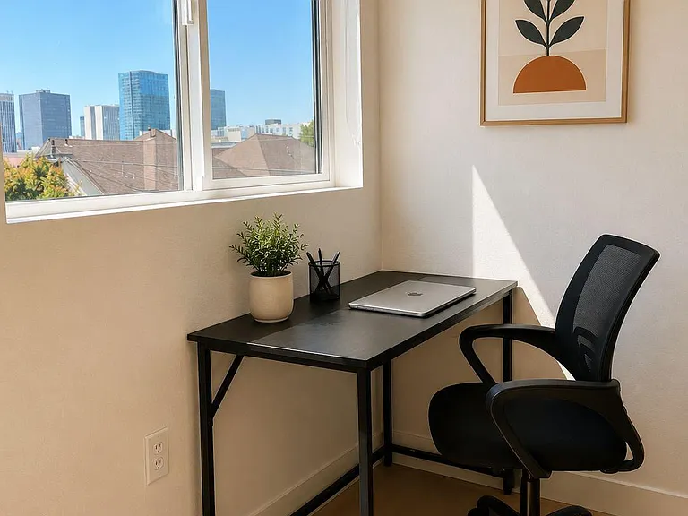 Dedicated work nook with a desk and task chair set by a large window, offering an open city-view backdrop.