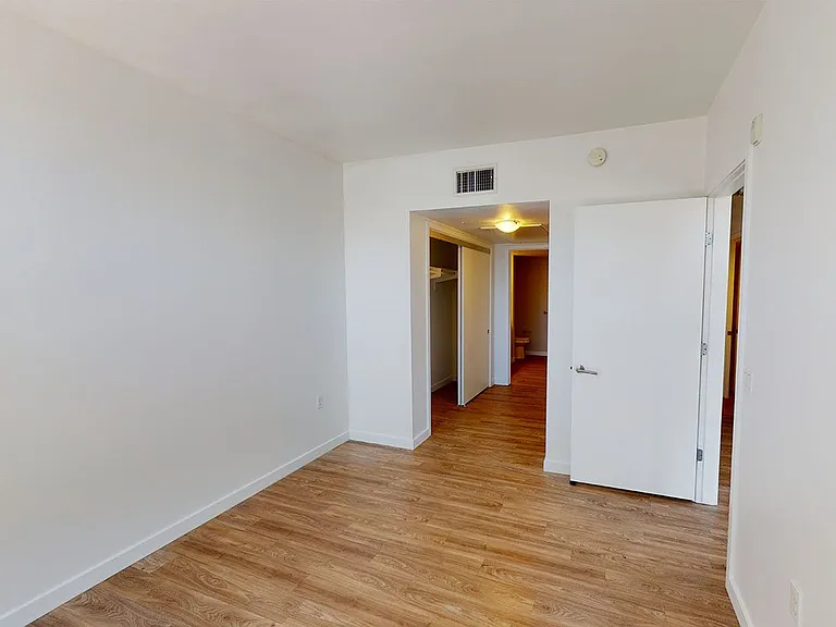 Spacious apartment bedroom with attached bathroom and wood-style flooring.