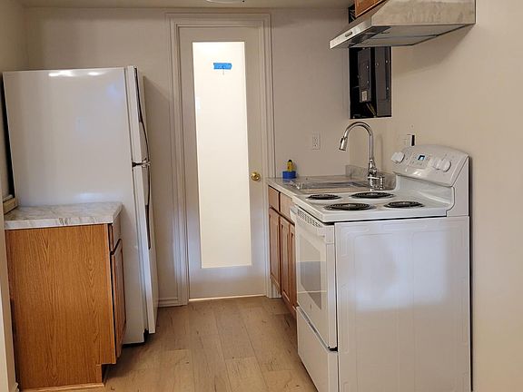 Kitchen area leading to bathroom door. Full size Refrigerator, electric stove, and kitchen sink. Microwave, toaster, blender, pretty much all the goodies a real kitchen needs.