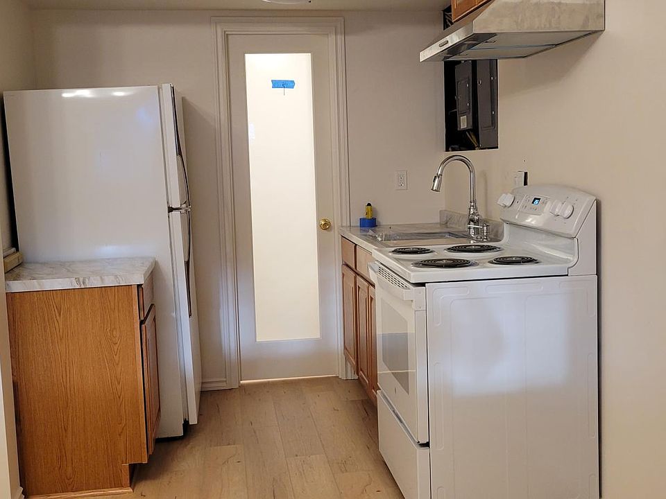 Kitchen area leading to bathroom door. Full size Refrigerator, electric stove, and kitchen sink. Microwave, toaster, blender, pretty much all the goodies a real kitchen needs.